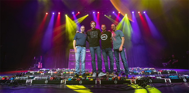 Pedal designers standing beside the baby they helped build at the world's largest pedalboard.